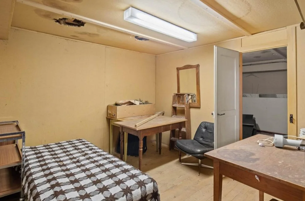 Ein heruntergekommenes Hotelzimmer, mit Loch in der Decke und alten Möbeln. 